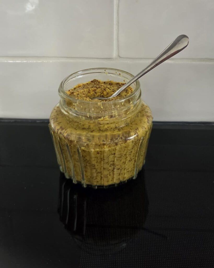 Zelfgemaakte grove mosterd in een glazen pot met lepel